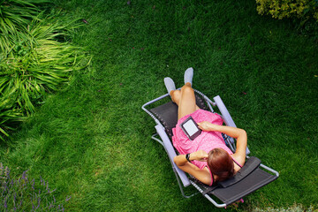 a woman in a red dress lies on a sun lounger on the grass and reads on an ebook reader