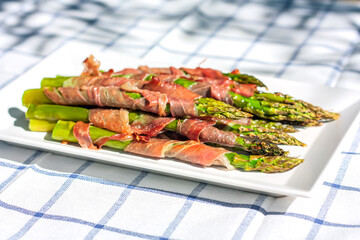 Green organic asparagus baked with bacon. Cooked Asparagus Officinalis on white plate on the table. Spring and summer vegetables for healthy snack. Recipe idea for branch.