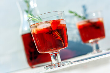 Two glasses and carafe with ice cube, pieces of watermelon, rosemary sprigs and red refreshing summer drink or red wine. Summertime concept. Selective focus.