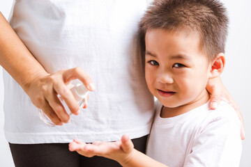 Fototapeta premium Closeup Asian Mother applying bottle pump dispenser sanitizer alcohol gel cleaning washing hands little child boy COVID-19 or coronavirus protection concept, isolated white background with copy space