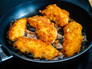 Breaded chicken breast nuggets frying in pan