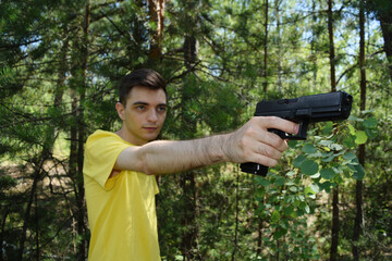 Young man in a yellow shirt shoots with a pistol in the forest