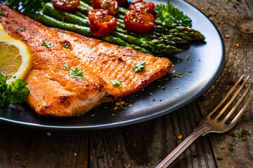 Fried salmon fillet with asparagus and cherry tomatoes served on black plate on wooden table