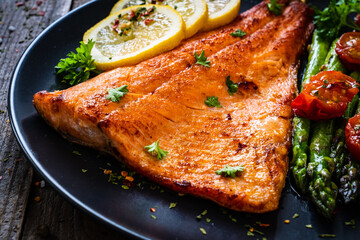 Fried salmon fillet with asparagus and cherry tomatoes served on black plate on wooden table