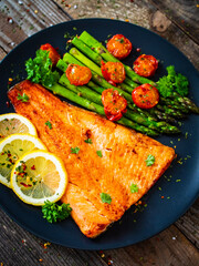 Fried salmon fillet with asparagus and cherry tomatoes served on black plate on wooden table