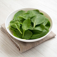 Fresh Baby Spinach in a white bowl on a white wooden background, side view.