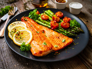 Fried salmon fillet with asparagus and cherry tomatoes served on black plate on wooden table