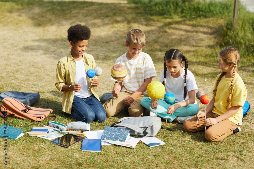 Wall mural full length portrait of multi-ethnic group o children sitting on green grass and holding model plane