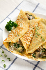 Savory Homemade Mushroom, Spinach and Cheese Crepes on a white plate on cloth, low angle view.