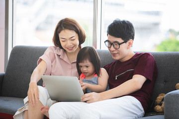 Young Asia family teaching daughter about laptop in the living room at home