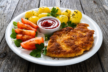 Breaded pork chop with boiled potatoes and vegetable salad on wooden background
