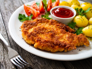 Breaded pork chop with boiled potatoes and vegetable salad on wooden background
