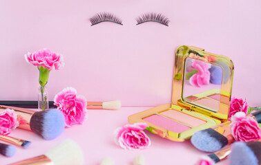 face with false eyelashes and flowers, premium makeup brushes on a colored pink background, creative cosmetics flat lay