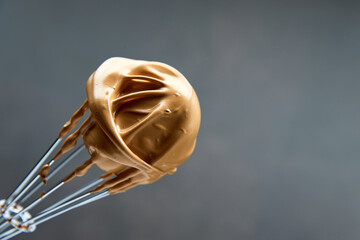 Whisk with fluffy creamy whipped coffee foam on a dark background. Trendy food and drink concept. Copy space..