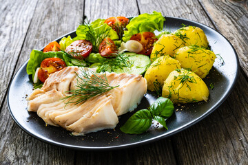Fish dish - fried cod fillet with vegetables on wooden table
