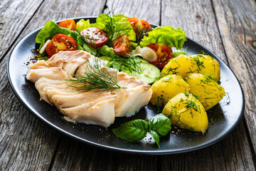 Fish dish - fried cod fillet with vegetables on wooden table
