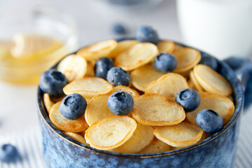 Blue Bowl of mini pancake cereal with blueberries, maple syrup and milk on concrete background. Tiny pancakes, new food trend concept. Cute healthy breakfast or snack. Recipe, menu.