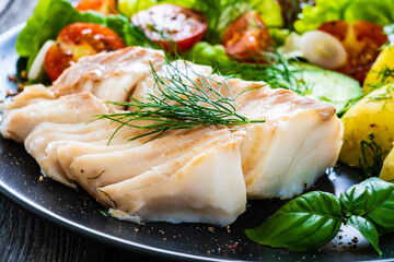 Fish dish - fried cod fillet with vegetables on wooden table
