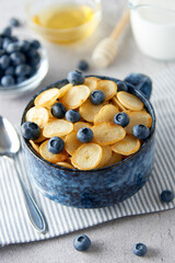 Blue Bowl of mini pancake cereal with blueberries, maple syrup and milk on concrete background. Tiny pancakes, new food trend concept. Cute healthy breakfast or snack. Recipe, menu.