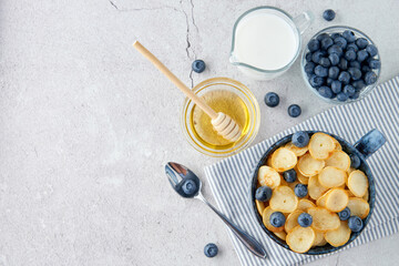 Blue Bowl of mini pancake cereal with blueberries, maple syrup and milk on concrete background. Tiny pancakes, new food trend concept. Cute healthy breakfast or snack. Recipe, menu.