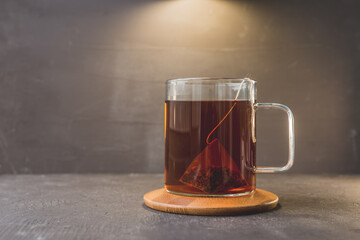 bag of tea in a glass mug on a wooden stand and a black table/bag of tea in a glass mug on a wooden stand and a black table. Copy space.