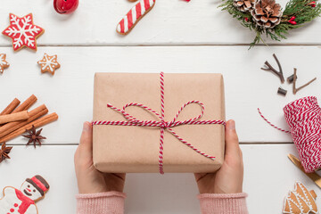 Female hands holding christmas gift box on wooden background with decorations.