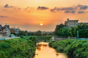 夕日に染まった横浜郊外の鶴見川と夕焼けの太陽