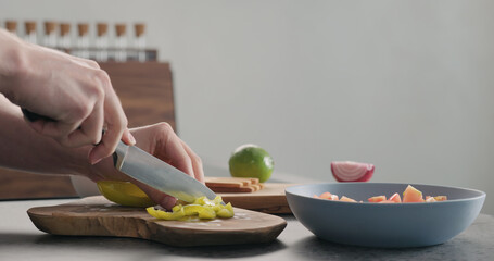 Man chopping yellow pepper on olive wood board for greek salad