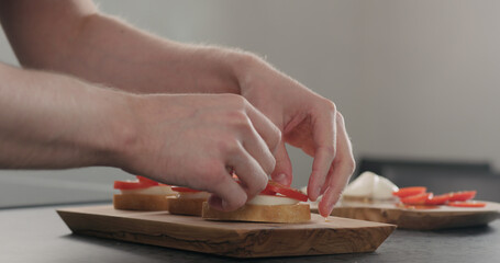 Obraz na płótnie Canvas man making bruschetta with tomatoes and mozzarella on wood board