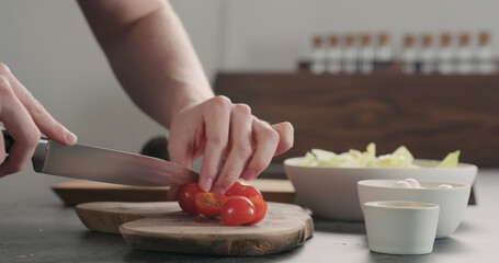 man cutting cherry tomatoes on olive wood board