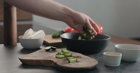 Fototapeta na wymiar Man chopping cucumber on olive wood board for greek salad