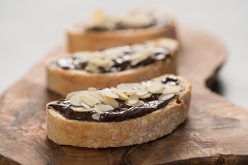 Rustic ciabatta with organic chocolate cream and almond flakes on olive wood board