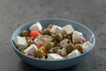 Classic greek salad in blue bowl on concrete countertp with copy space