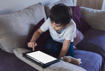 Cropped shot kid sitting on sofa watching cartoons on tablet,6-7 year old boy playing game on touch...