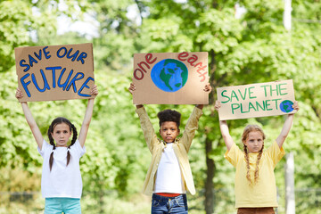 Waist up portrait of three children holding signs with SAVE PLANET SAVE FUTURE while protesting for...