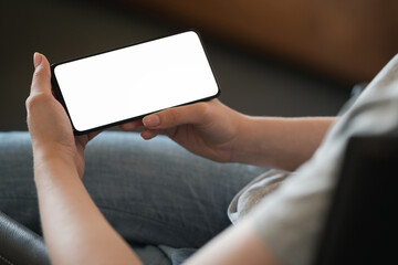 Une jeune femme tient un smartphone avec un écran blanc tout en étant assise sur une chaise