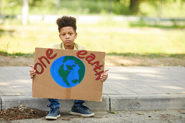 Full length portrait of African-American boy holding sign with ONE EARTH and looking at camera...