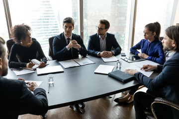 Concentrated multiracial business people in formal suits sitting in negotiations table, involved in brainstorming process in boardroom, discussing working issues, developing strategy indoors.