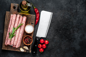 Thin raw meat sausages on a stone background with copy space for your text.
