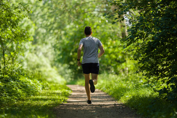 One young, adult man running in forest on natural trail in sunny summer day. Daily active...