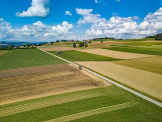 vue depuis un drone dans un temps ensoleillé avec des nuages blancs dans le fond sur les cultures de la campagne vaudoise en suisse-romande avec une ferme au loin