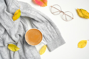 Fototapeta na wymiar Cup of coffee, knitted sweater, fallen leaves, glasses on white table. Autumn hygge home desk concept. . Autumn composition concept.Top view, flat lay, overhead