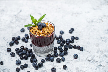Plakat Healthy breakfast or morning snack with chia seeds pudding, granola, muesli and blueberries on white stone background, vegetarian food, diet and health concept.