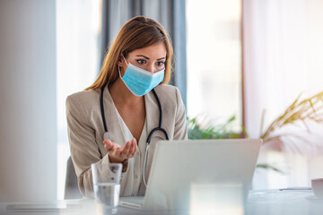 Fototapeta na wymiar Female doctor counseling, helping patient online, medic using laptop for video call. Online doctor with a protective mask tutoring over the internet. Mid adult female doctor working in office