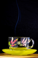 Glass cup with a floral pattern on a green saucer. Сurly smoke