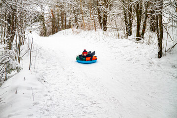 A boy rolls down a slide on snowtubes in the winter in the forest. Children's games in the snow.