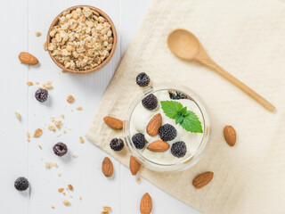 Yogurt with berries and almonds in a glass on a white table.