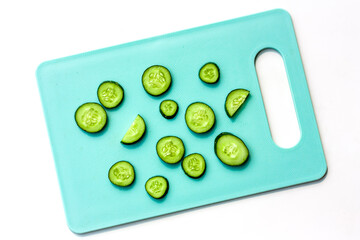 Obraz na płótnie Canvas Cucumber creative layout. Slices of fresh cucumbers on turquoise cutting board on white background. Top view. Food knolling and abstracts elements.