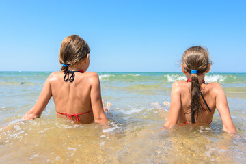 Children sit in the water on the coast and look into the distance