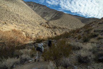 Two male backpackers hike up the Cottonwood Canyon Trail, part of the popular Cottonwood Canyon- Marble Canyon backpacking loop trail in Death Valley National Park in California